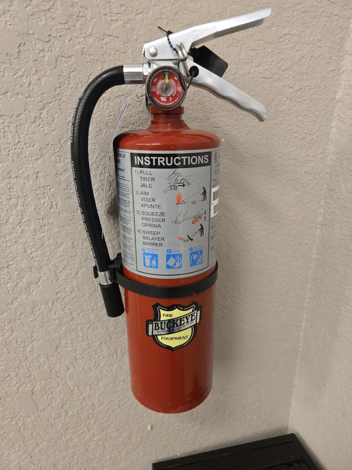 A wall-mounted fire extinguisher with a current inspection gauge and instruction label